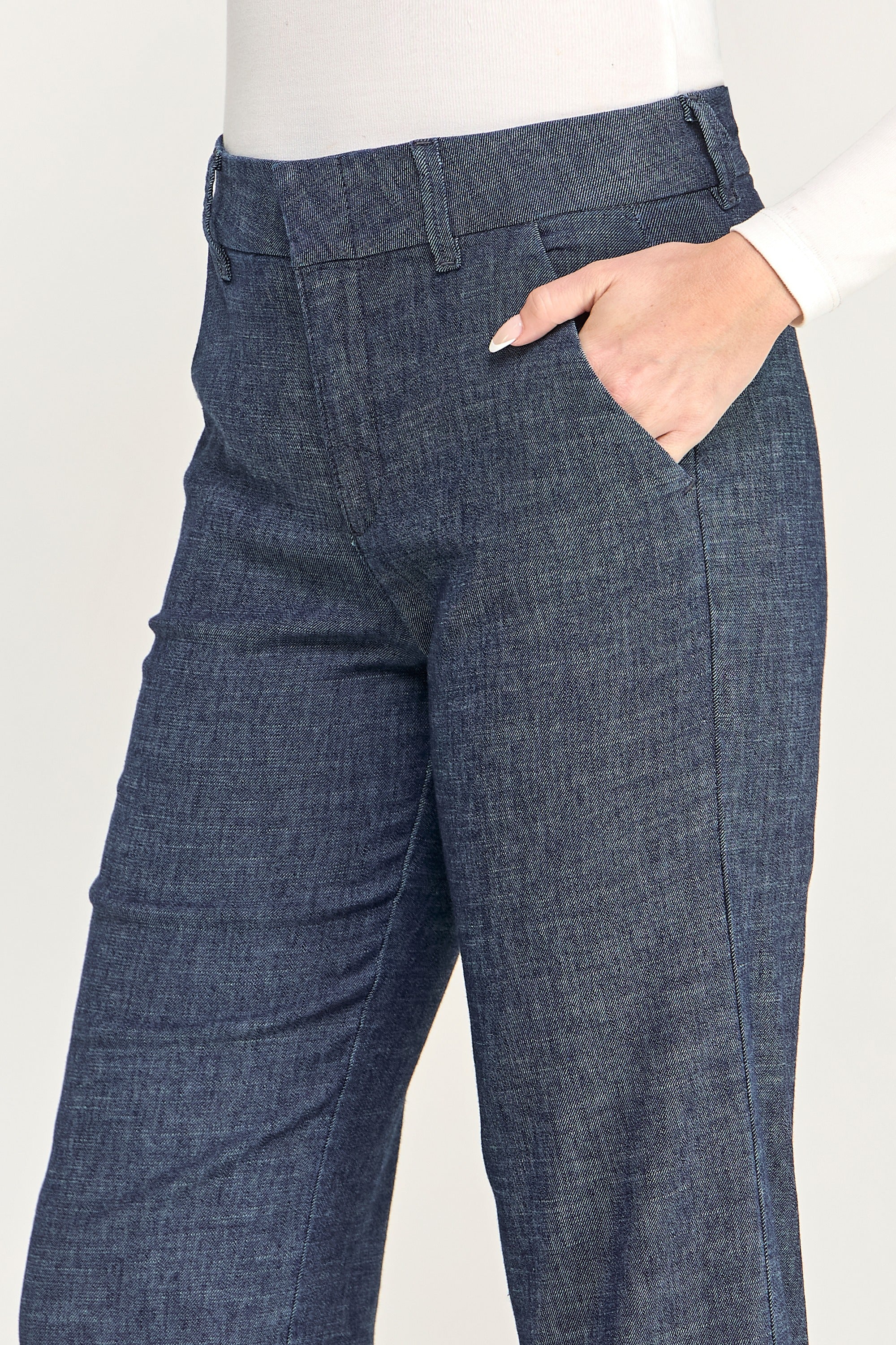 Close-up of a person wearing dark blue denim-style pants with a side pocket and hand in pocket, against a light neutral background.
