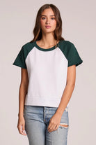 Woman wearing a green and white baseball-style shirt with blue jeans on a plain background