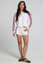 Woman wearing a white Adidas tracksuit with red stripes on a plain background