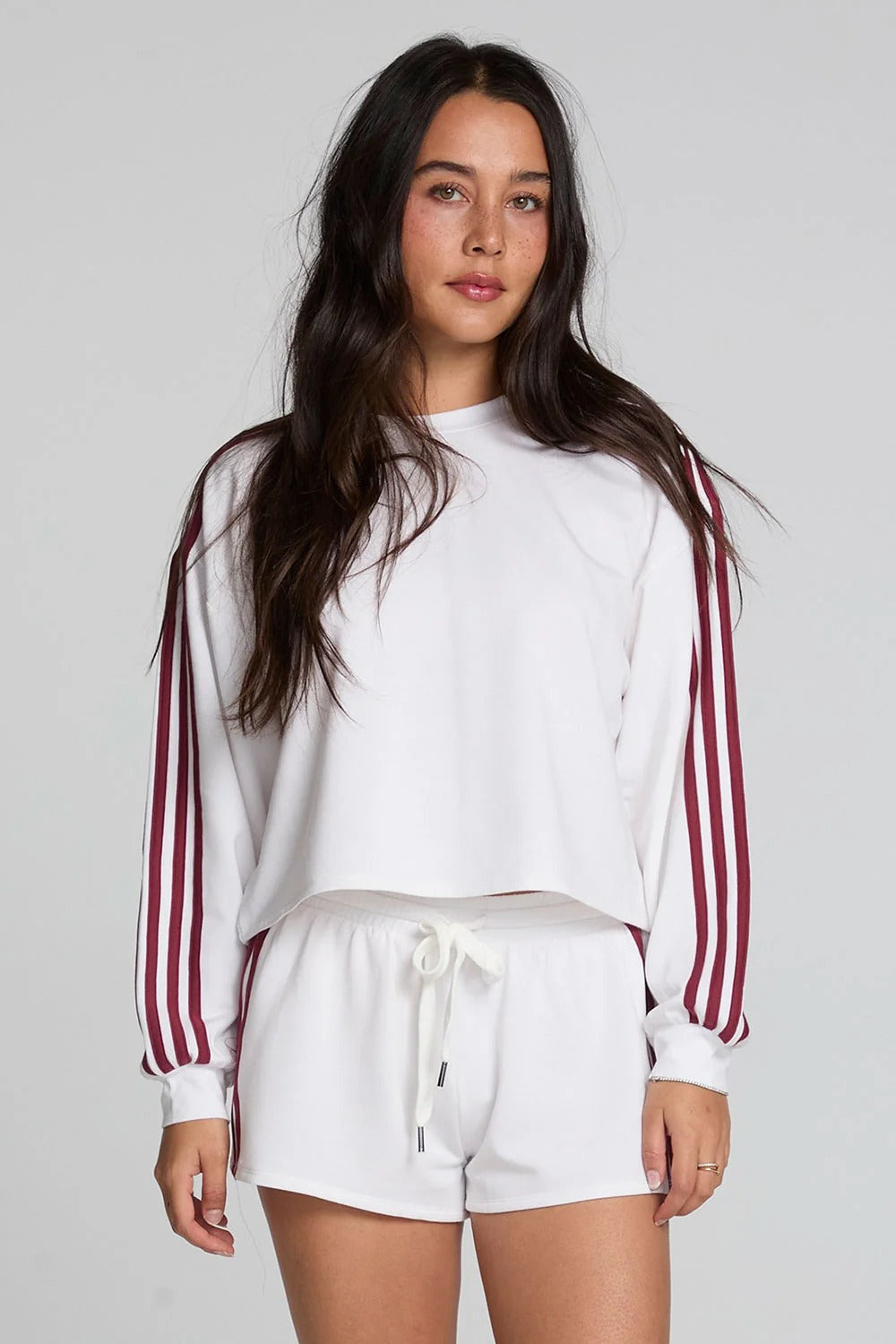 Woman wearing a white sweatshirt with red stripes and white shorts on a plain background