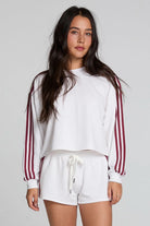 Woman wearing a white sweatshirt with red stripes and white shorts on a plain background