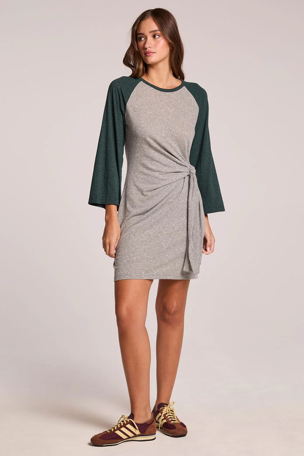 Woman wearing a gray dress with green sleeves on a plain background