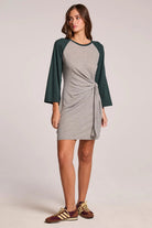 Woman wearing a gray dress with green sleeves on a plain background