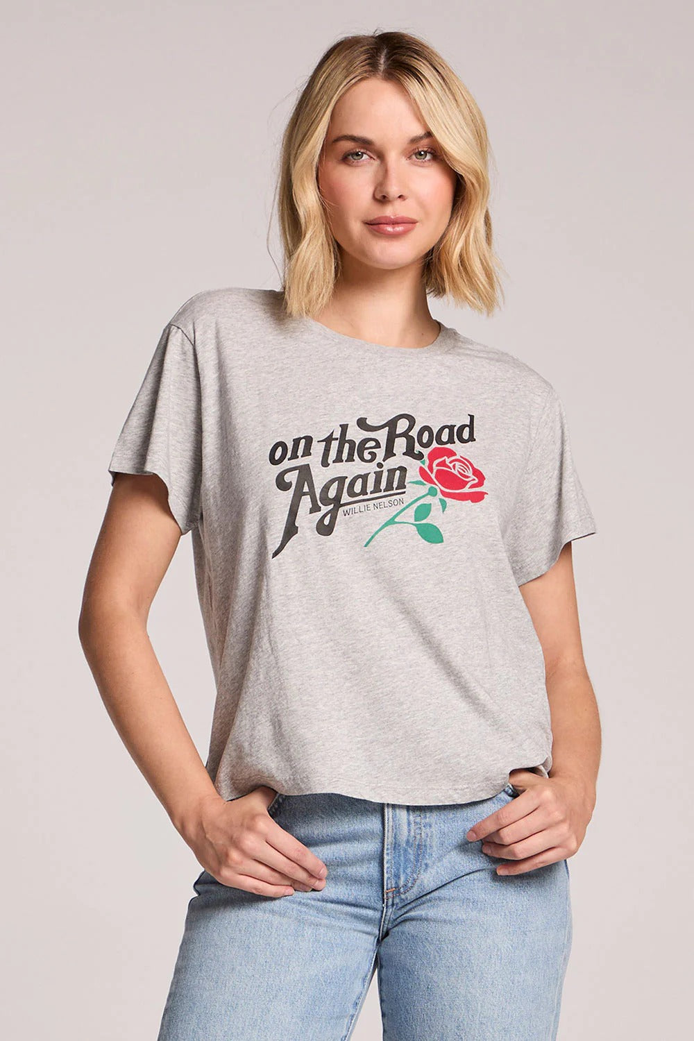 Woman wearing a gray t-shirt with 'On the Road Again' and a rose graphic on a plain background