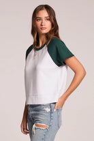 Woman wearing a white and green baseball tee with ripped jeans on a plain background
