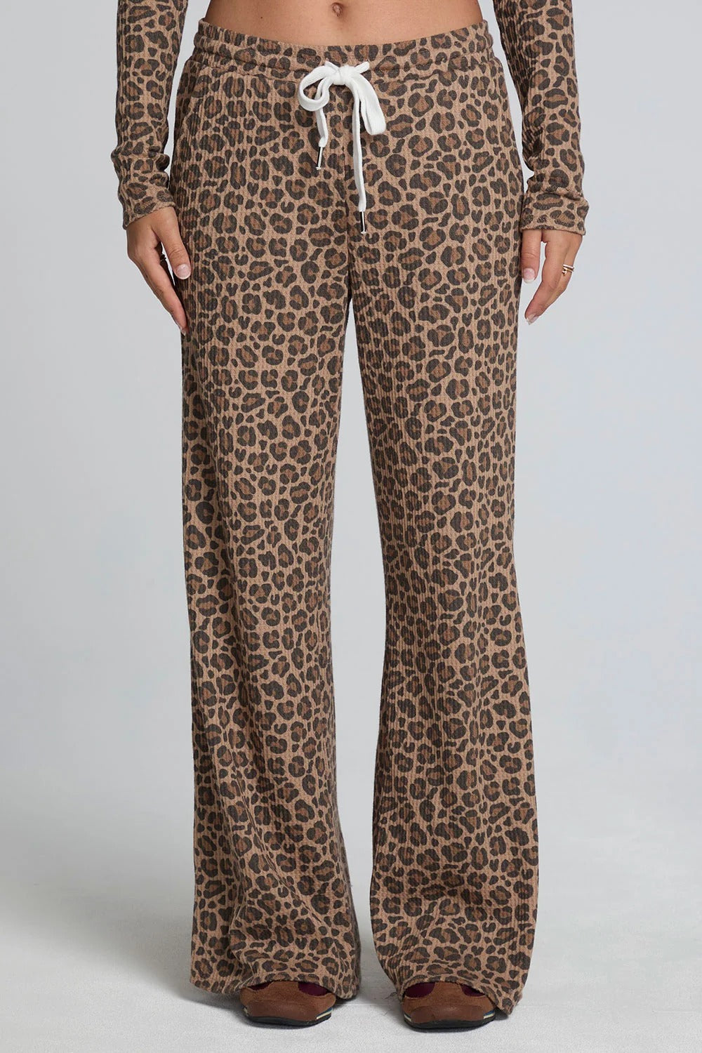 A person wearing leopard-print wide-leg pants with a white drawstring waist, paired with a matching long-sleeve top, shown against a light gray studio background.