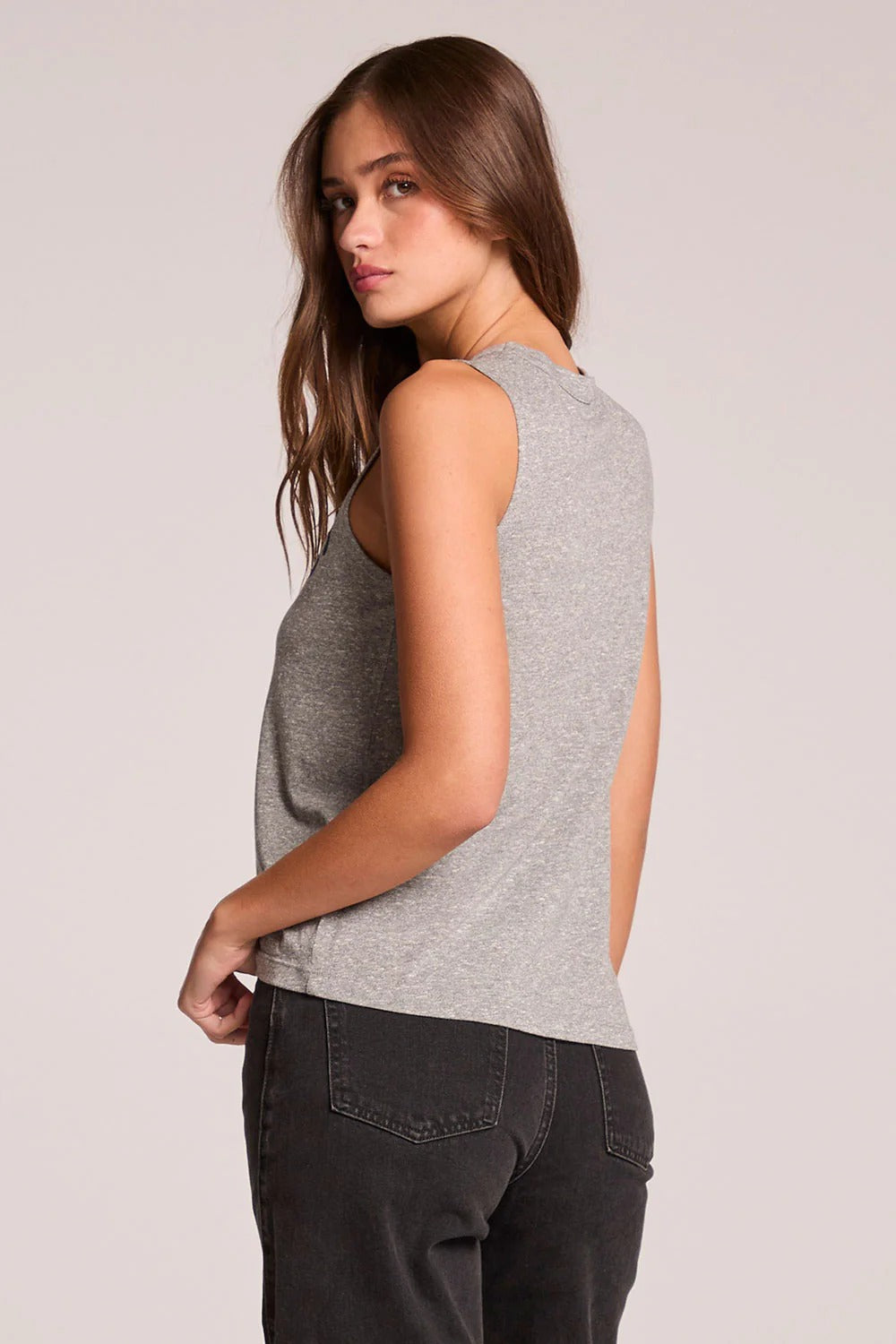 Woman wearing a gray sleeveless top and dark pants on a light background