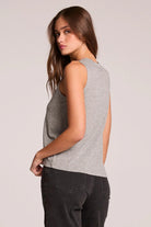 Woman wearing a gray sleeveless top and dark pants on a light background