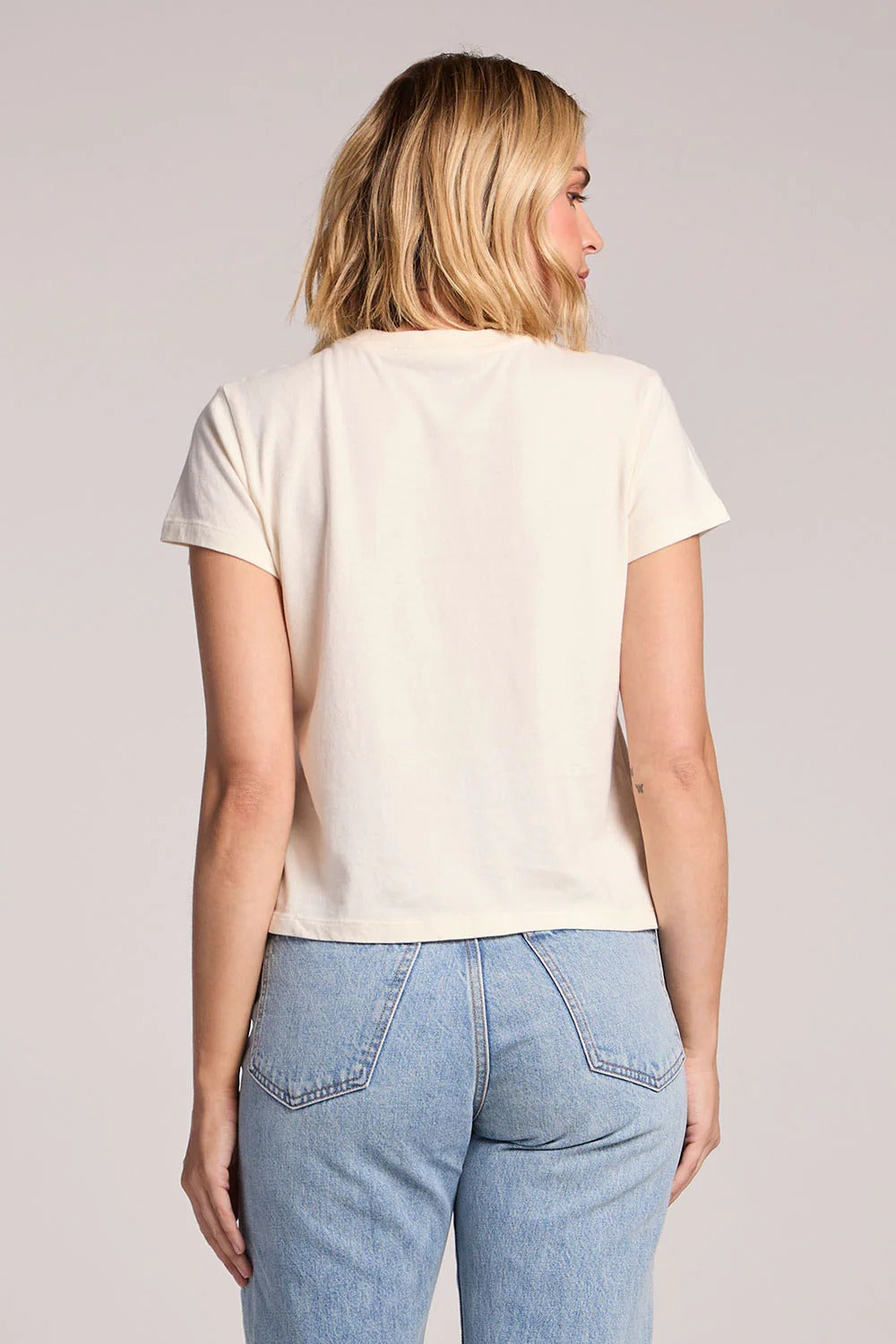 Person wearing a beige t-shirt and blue jeans on a plain background