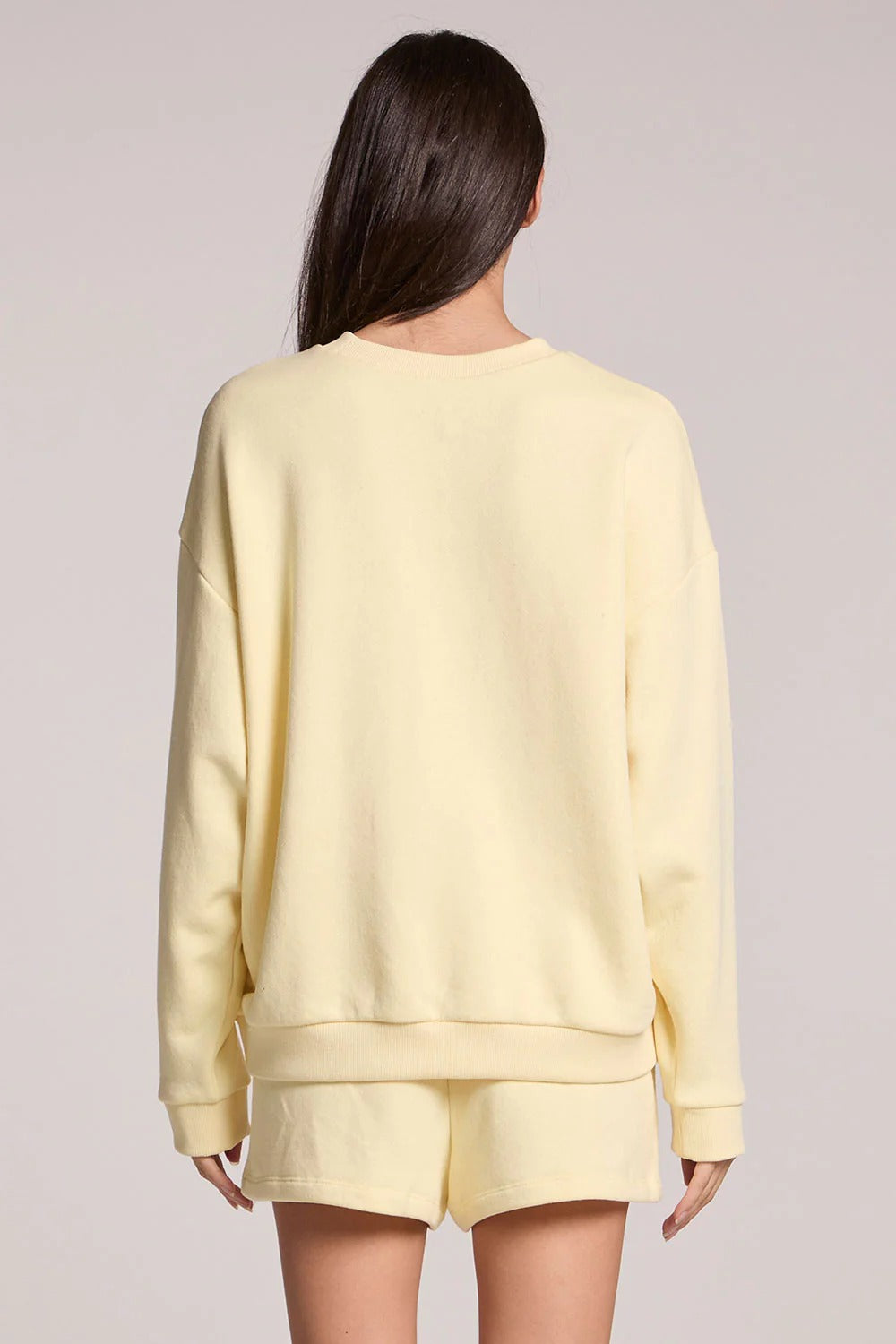 Person wearing a light yellow sweatshirt and shorts set on a plain background