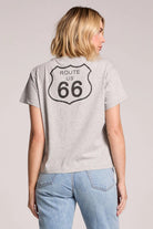 Person wearing a gray t-shirt with Route 66 design on the back, standing against a plain background.