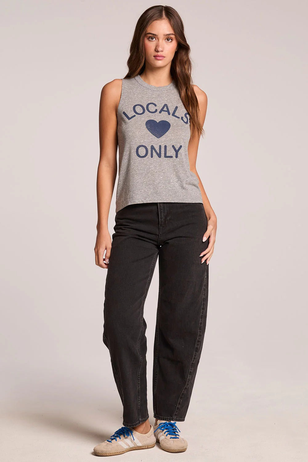 Woman wearing a sleeveless shirt with 'Locals Only' text and black pants on a plain background