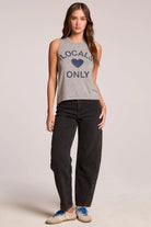 Woman wearing a sleeveless shirt with 'Locals Only' text and black pants on a plain background