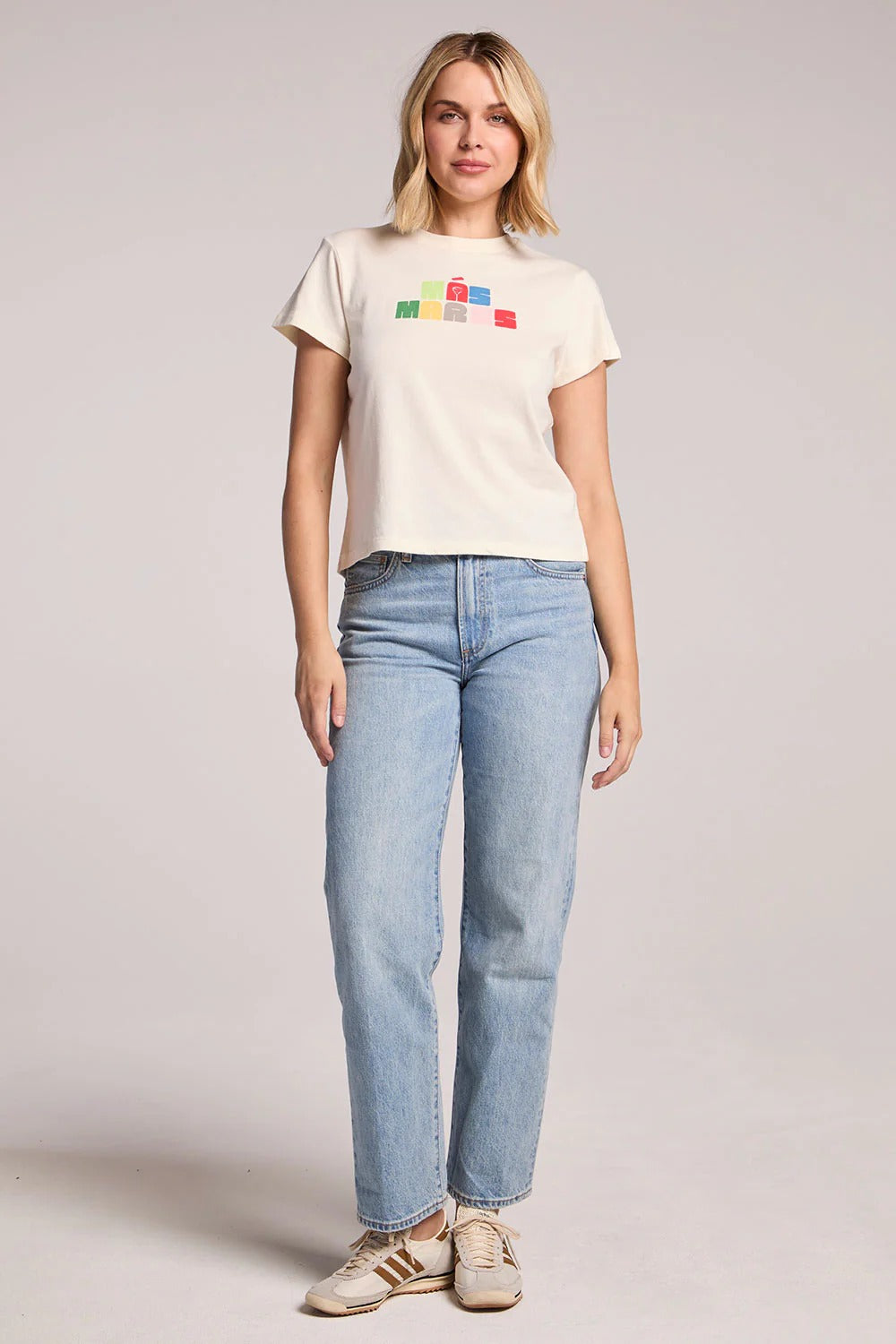 Woman wearing a white t-shirt with colorful graphics and blue jeans on a plain background