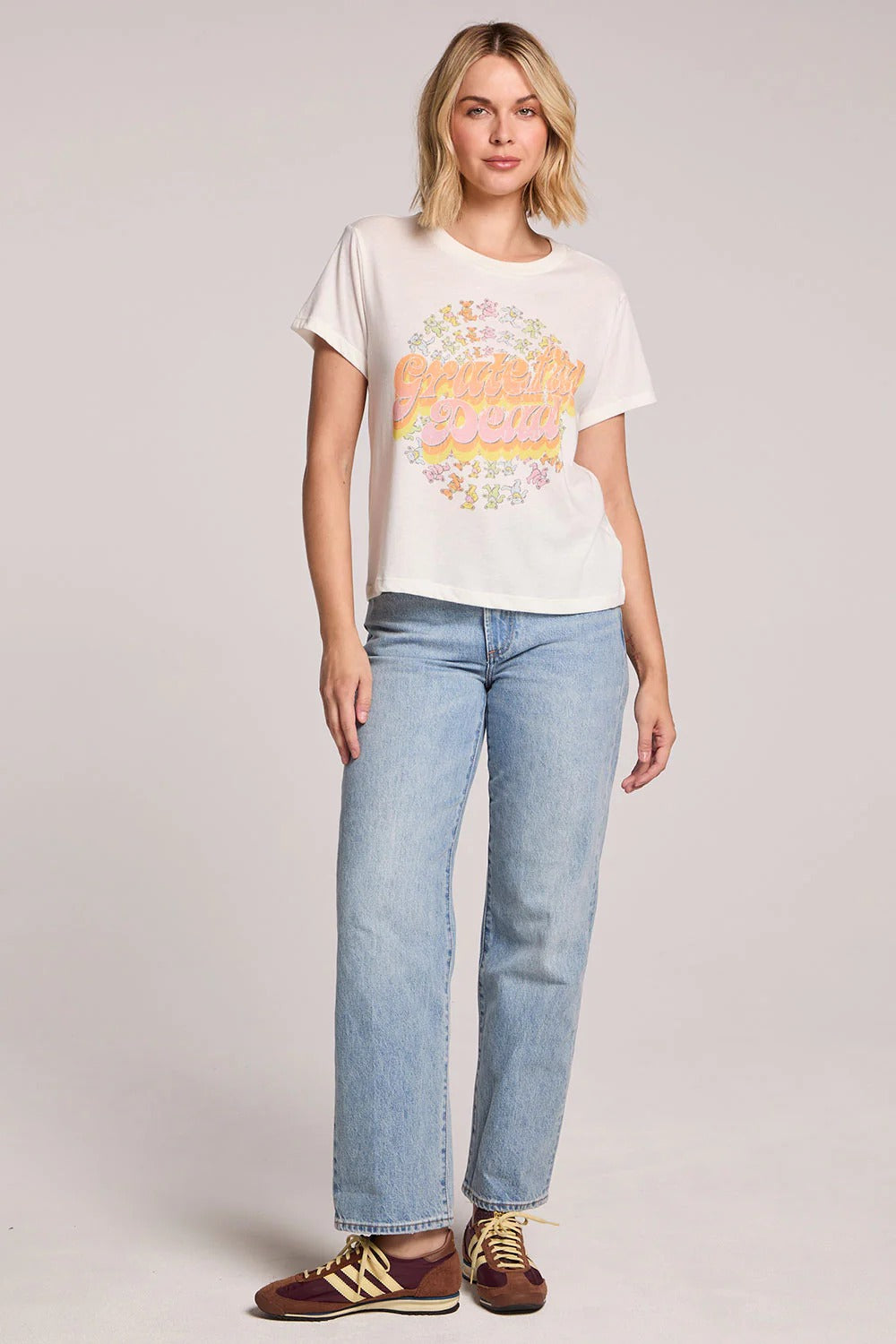 Woman wearing a white t-shirt with colorful graphics and light blue jeans on a plain background
