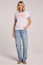 Woman wearing a white t-shirt with colorful graphics and blue jeans on a plain background