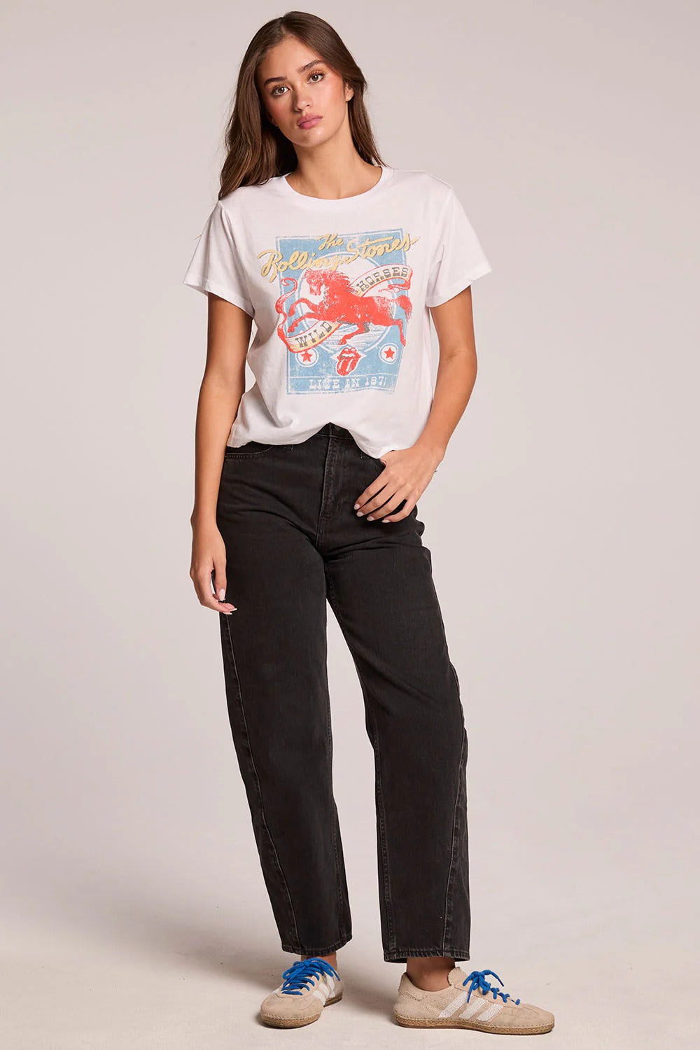 Woman wearing a white t-shirt with a graphic design and black jeans on a plain background