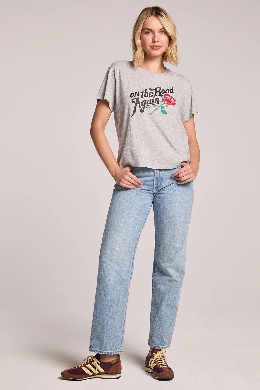 Woman wearing a gray t-shirt with a graphic and text, paired with light blue jeans on a plain background