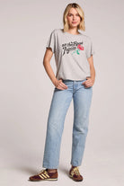 Woman wearing a gray t-shirt with a graphic and text, paired with light blue jeans on a plain background