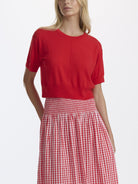 Woman wearing a red top and red and white checkered skirt on a white background