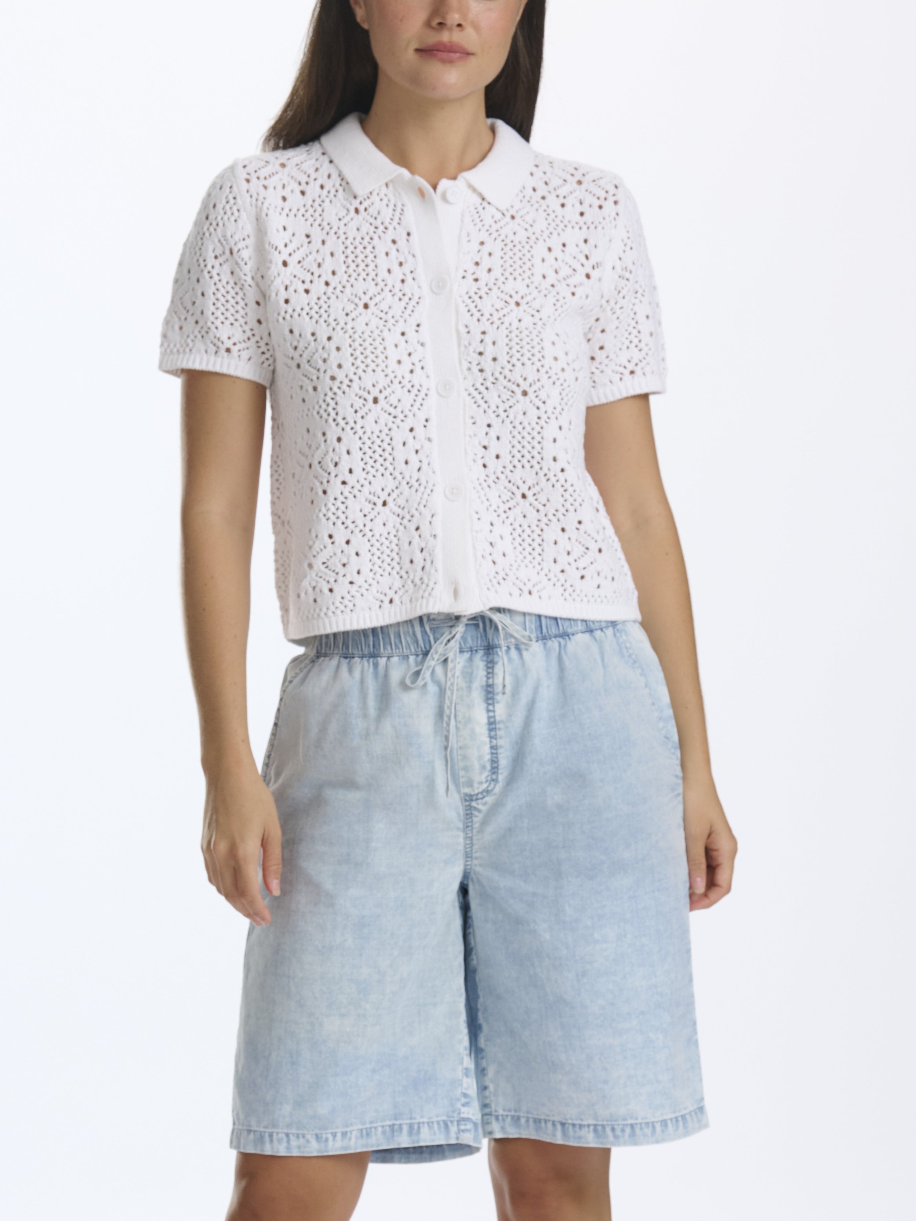 Woman wearing a white lace top and light blue denim shorts on a white background