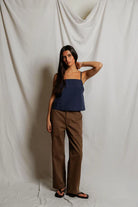 Woman wearing a blue top and brown pants against a plain white background