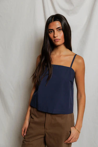 Woman wearing a navy blue top and brown pants against a plain background