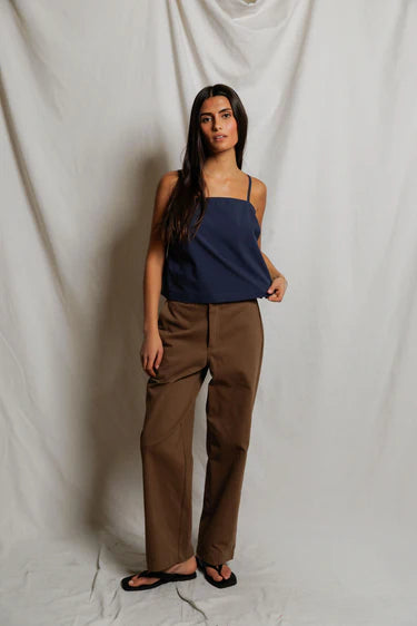 Woman wearing a navy top and brown pants against a white backdrop