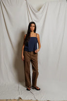 Woman wearing a navy top and brown pants against a plain white background