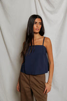 Woman wearing a navy blue top and brown pants against a white background
