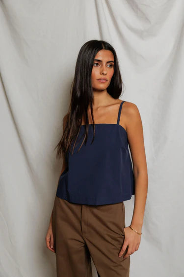 Woman wearing a navy blue top and brown pants against a white background