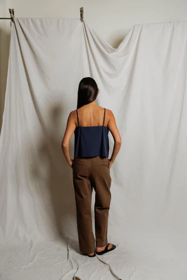 Person wearing a navy top and brown pants standing against a white curtain.