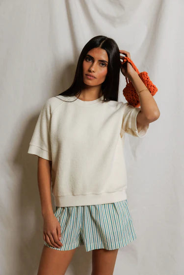 Woman wearing a white oversized sweatshirt and striped shorts against a plain background