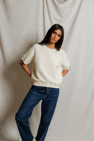 Woman wearing a white sweater and blue jeans against a plain background