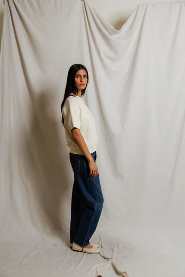 Woman standing against a plain white curtain