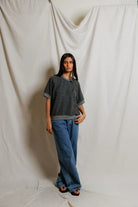 Person wearing a dark gray t-shirt and blue jeans standing against a plain white background