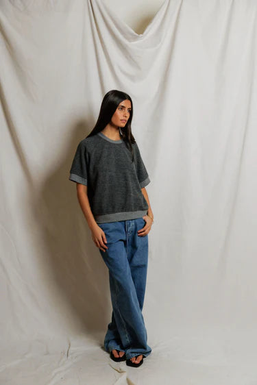 Person wearing a dark gray sweater and blue jeans against a plain background