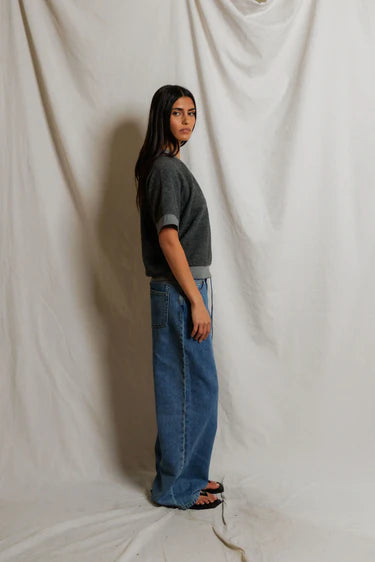 Person wearing a gray sweater and blue jeans standing against a plain white background