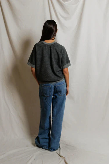Person wearing a dark gray t-shirt and blue jeans standing against a plain white background