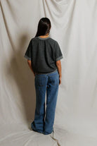Person wearing a dark gray t-shirt and blue jeans standing against a plain white background