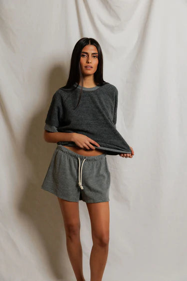 Woman wearing a gray oversized shirt and shorts set against a plain background