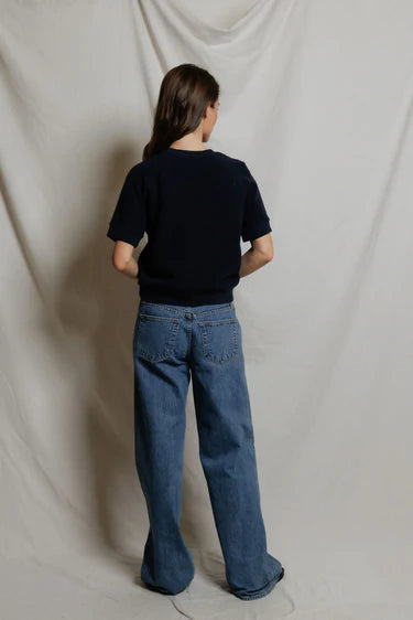 Person wearing a black shirt and blue jeans standing against a plain white background