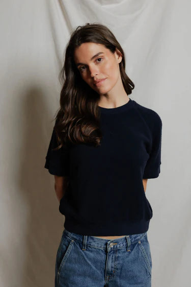 Woman wearing a navy sweater and blue jeans against a plain background