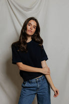 Woman wearing a black top and blue jeans against a plain background