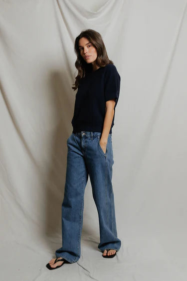 Person wearing a black shirt and blue jeans against a plain background