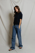Person wearing a black shirt and blue jeans against a plain background