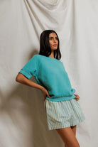 Woman wearing a teal sweater and striped skirt against a plain background