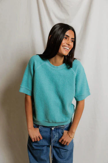 Woman wearing a teal sweater and blue jeans against a plain background