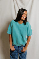 Woman wearing a teal sweater and blue jeans against a plain background