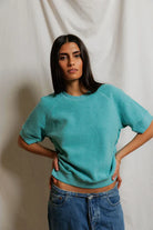 Woman wearing a teal sweater and blue jeans against a plain background
